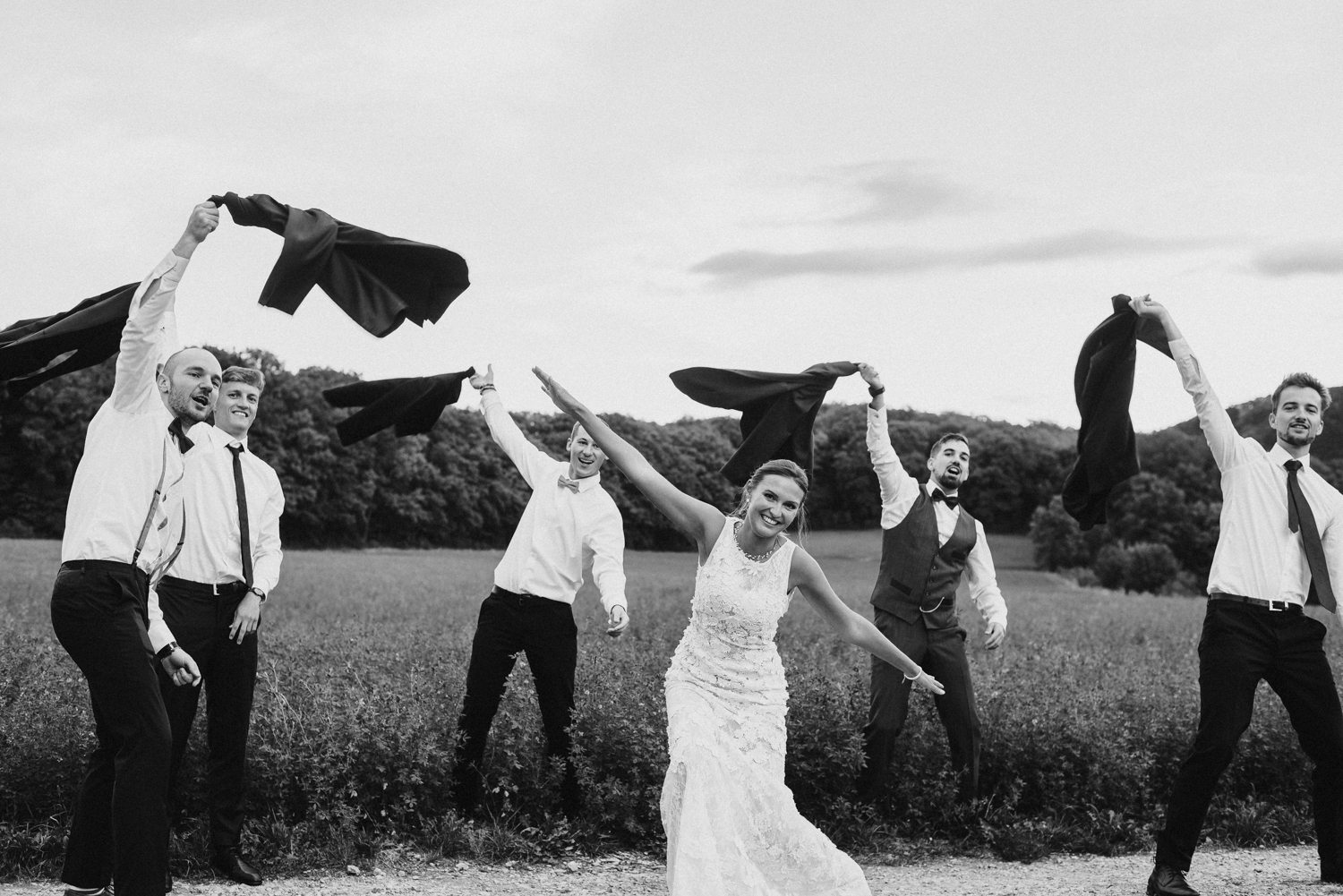 Gruppenbild mit Braut in der Mitte und Männer wehen mit ihren Jacken in die Luft